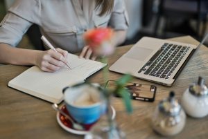 Stock image of a freelancer working on a project with a notebook, laptop, and coffee on their desk. It's to illustrate the article 6 Smart Ways to Branch Out as a Freelance Writer