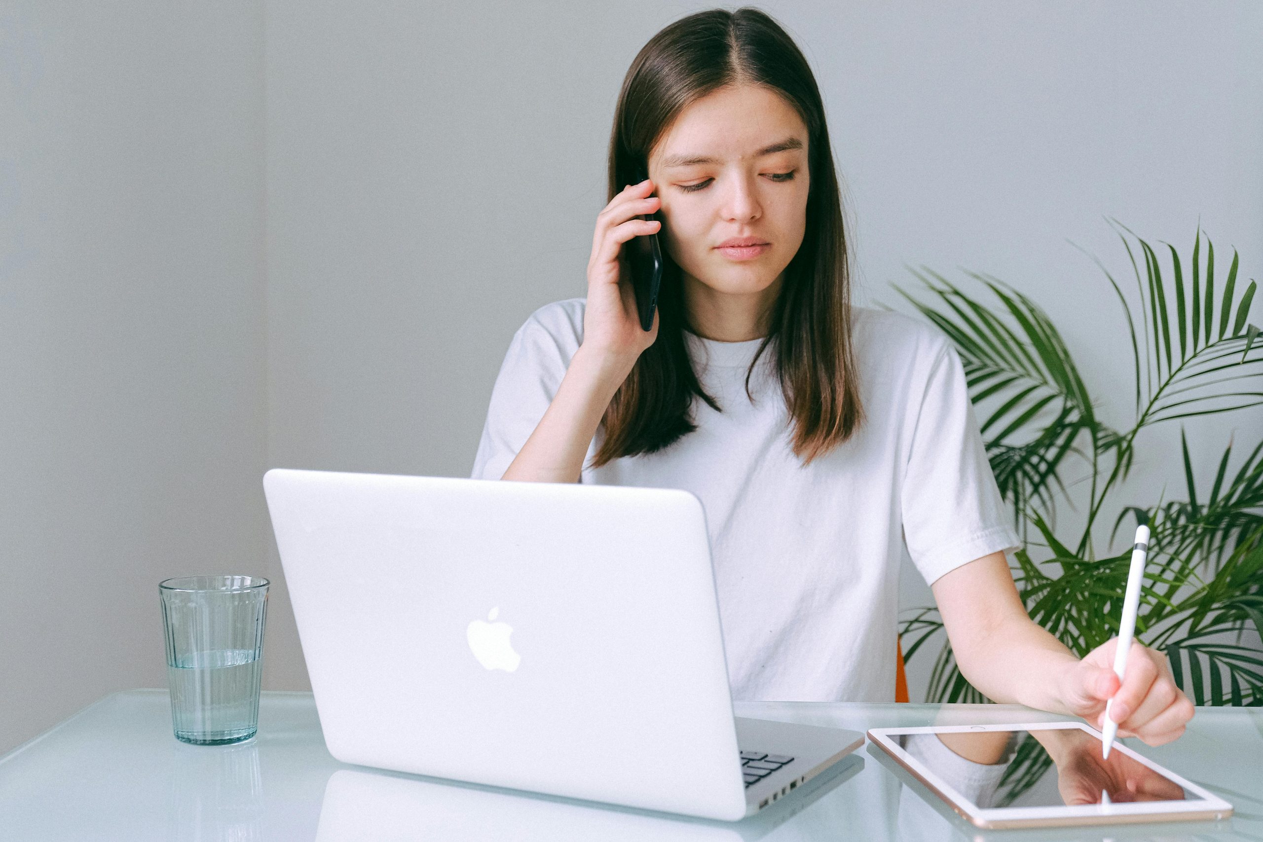 Stock image of a woman sitting in front of a laptop while talking on a mobile and writing on a tablet. This is to demonstrate growing your freelance writing business