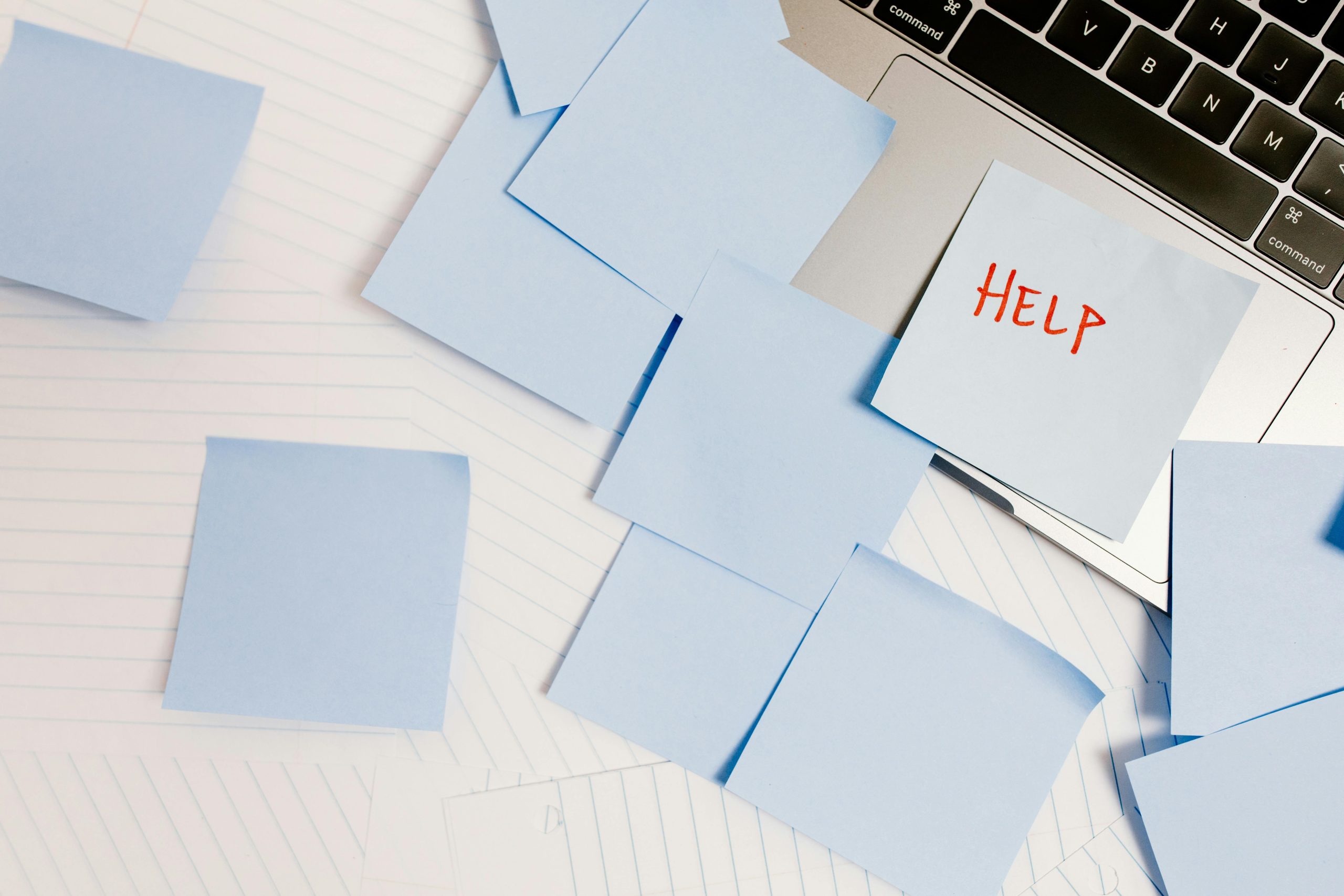 Overhead shot of blue sticky notes all over a desk with "Help" written on one.